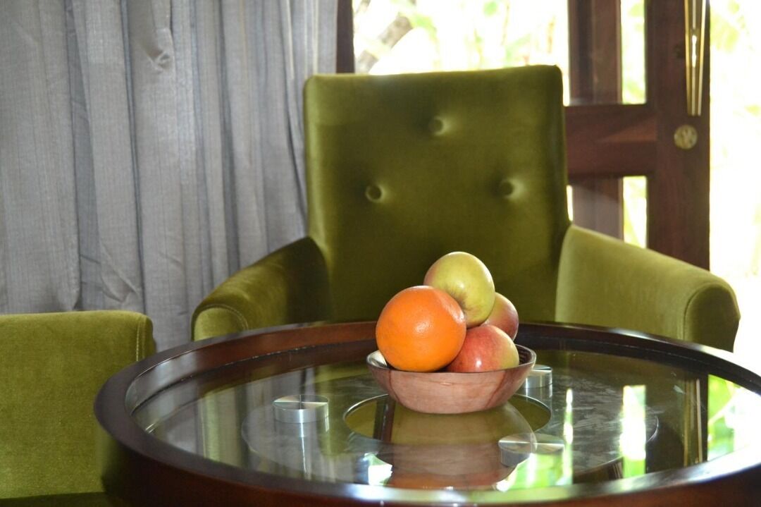A round glass table with a wooden bowl containing apples and an orange.
