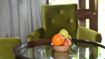 A round glass table with a wooden bowl containing apples and an orange.