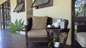 A wicker chair with a beige cushion, a small round table with a potted plant, and a tray with teapots and a box of red grape juice. - Staybridge Riverside & Spa (Francistown)