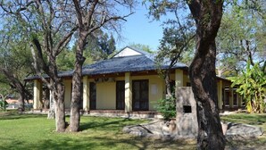 A yellow building with a tiled roof, surrounded by trees and a grassy lawn. - Staybridge Riverside & Spa (Francistown)