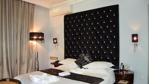 A hotel room with a large bed, a headboard with lights, bedside lamps, a bedside table, and a wall-mounted phone. - Staybridge Riverside & Spa (Francistown)