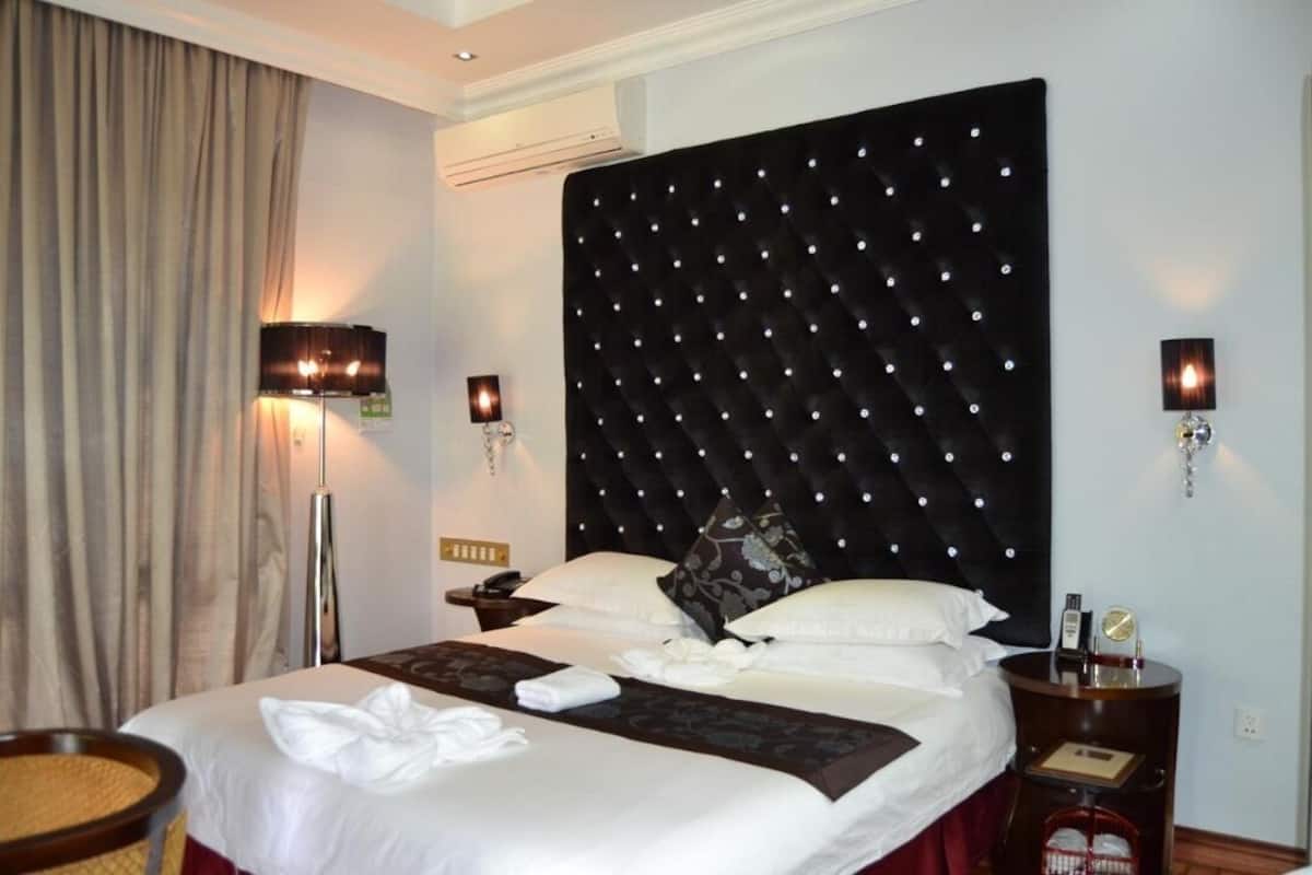 A hotel room with a large bed, a headboard with lights, bedside lamps, a bedside table, and a wall-mounted phone.