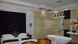 A hotel room with a large bed, a sitting area with chairs, a bathtub, and a shower area. - Staybridge Riverside & Spa (Francistown)