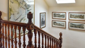 Eine Treppe mit Holzbalkonen, ein großes gerahmtes Gemälde und mehrere kleinere gerahmte Kunstwerke an der Wand.