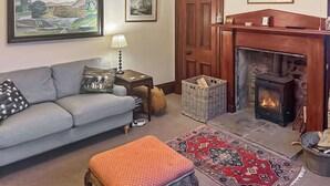 Ein gemütliches Wohnzimmer mit einer Couch, einem Kamin, einem Teppich und gerahmten Kunstwerken an den Wänden.