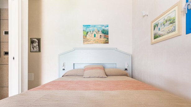 Une chambre à coucher avec un lit, une tête de lit, un tableau et une photographie encadrée accrochée au mur.