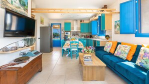 Eine moderne Küche mit blauen Schränken, ein Essbereich mit Tisch und Stühlen sowie ein Wohnzimmer mit blauem Sofa und bunten Kissen.