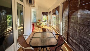 A corridor with a glass door, a table with chairs, and a view of a garden through large windows. - Villa Poisson dans L'eau (Trou-aux-Biches)