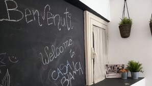 Quadro negro com a inscrição 'Welcome to Casa Blanca', uma porta branca e um balcão com plantas em vasos e uma foto emoldurada.