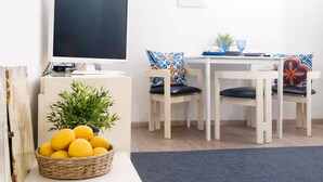 Uma sala de estar moderna com uma televisão de tela plana, uma mesa de jantar com cadeiras, um cesto de limões e obras de arte emolduradas na parede.