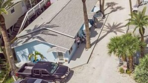 Una zona residenziale costiera con vista sulla spiaggia, che include un edificio a più piani e diverse case singole con palme.