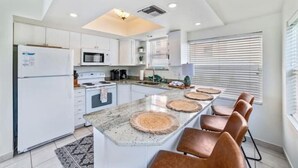 Una cucina moderna con pensili bianchi, un'isola centrale con sgabelli, un forno a microonde e un frigorifero.