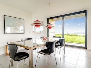 A dining area with a glass table, black chairs, a red pendant light, and a large window with a view of the sea.