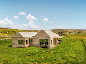 A modern house with a sloped roof, large windows, and a grassy yard.