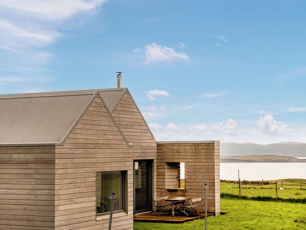 A modern wooden cabin with a sloped roof, a large window, and a picnic table outside.