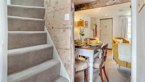 A staircase leading to a dining area with a table set for two, a yellow armchair, and a door in the background.