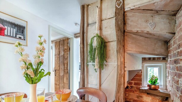 A rustic interior with a wooden staircase, a dining table set with plates and glasses, and a framed picture on the wall.
