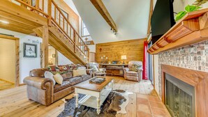 A spacious living room with a wooden staircase, a fireplace, and a high ceiling. - Ruidoso Cabin w/ Deck + Views: 4 Mi to Winter Park (Ruidoso)