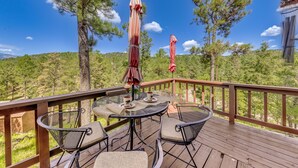 A wooden deck with outdoor furniture, including chairs and a table, overlooking a forested area. - Ruidoso Cabin w/ Deck + Views: 4 Mi to Winter Park (Ruidoso)