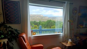 A room with a large window offering a view of a mountainous landscape. There is a brown leather chair and a small table with a tissue box and decorative items. - Cliff View Hacienda - Wild & Serene (Camp Verde)