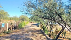A paved pathway flanked by trees and a wooden fence, leading towards a distant structure. - Cliff View Hacienda - Wild & Serene (Camp Verde)