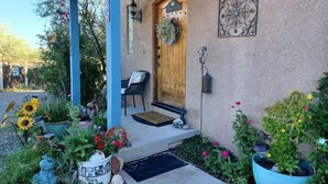 A house with a wooden front door, a porch with a chair, and various potted plants and flowers around the entrance. - Cliff View Hacienda - Wild & Serene (Camp Verde)