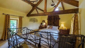 Une chambre avec un plafond haut, des poutres apparentes, un lit à baldaquin, une table de chevet, une lampe et une chaise.