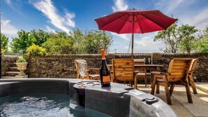 Un bain à remous, une bouteille de champagne, un parasol rouge et des chaises en bois.