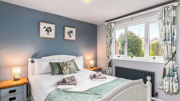 A bedroom with a bed, bedside tables, a window with curtains, and a radiator.