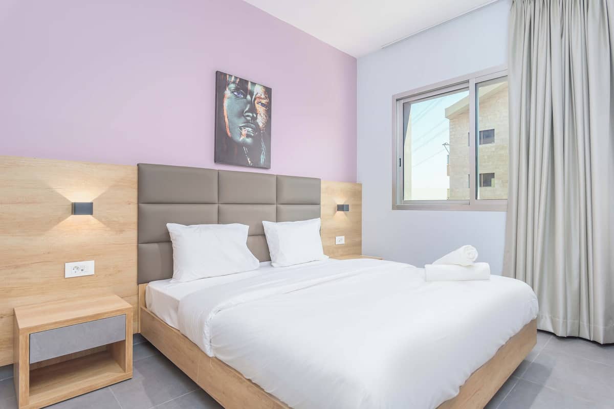 A modern hotel room with a large bed, a nightstand, a wall-mounted light, and a window with curtains.