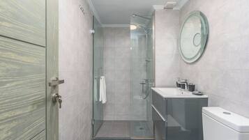 Un baño moderno con cabina de ducha de vidrio, lavabo con espejo e inodoro.