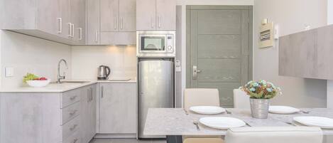 Una cocina moderna con microondas integrado, refrigerador y lavamanos. Hay un comedor con una mesa lista para dos personas, y una puerta que da a otra habitación.