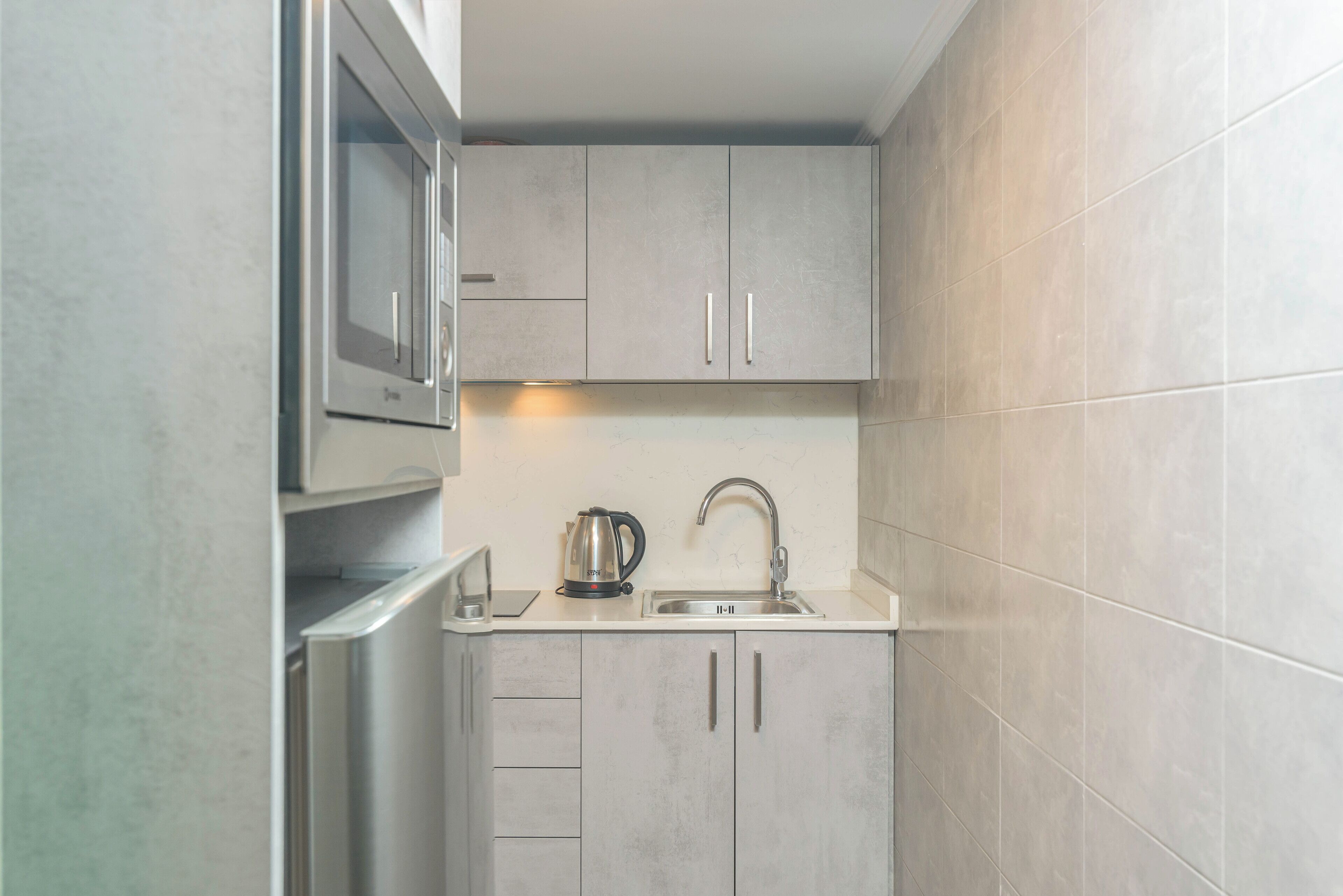 Una cocina compacta con microondas integrado, hervidor y lavabo.