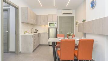 Una cocina moderna con zona de comedor, que incluye un microondas, refrigerador y una mesa de comedor con sillas naranjas.