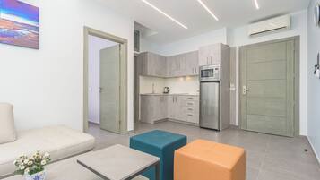 Una cocina moderna con armarios grises, un refrigerador de acero inoxidable y un microondas. Hay un sofá color beige y una mesita con un jarrón de flores.