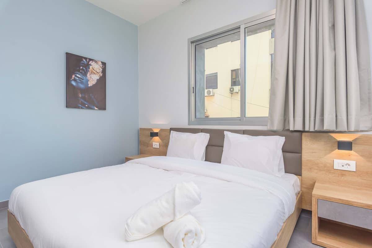 A neatly made bed with white linens, a rolled towel, and a painting on the wall.