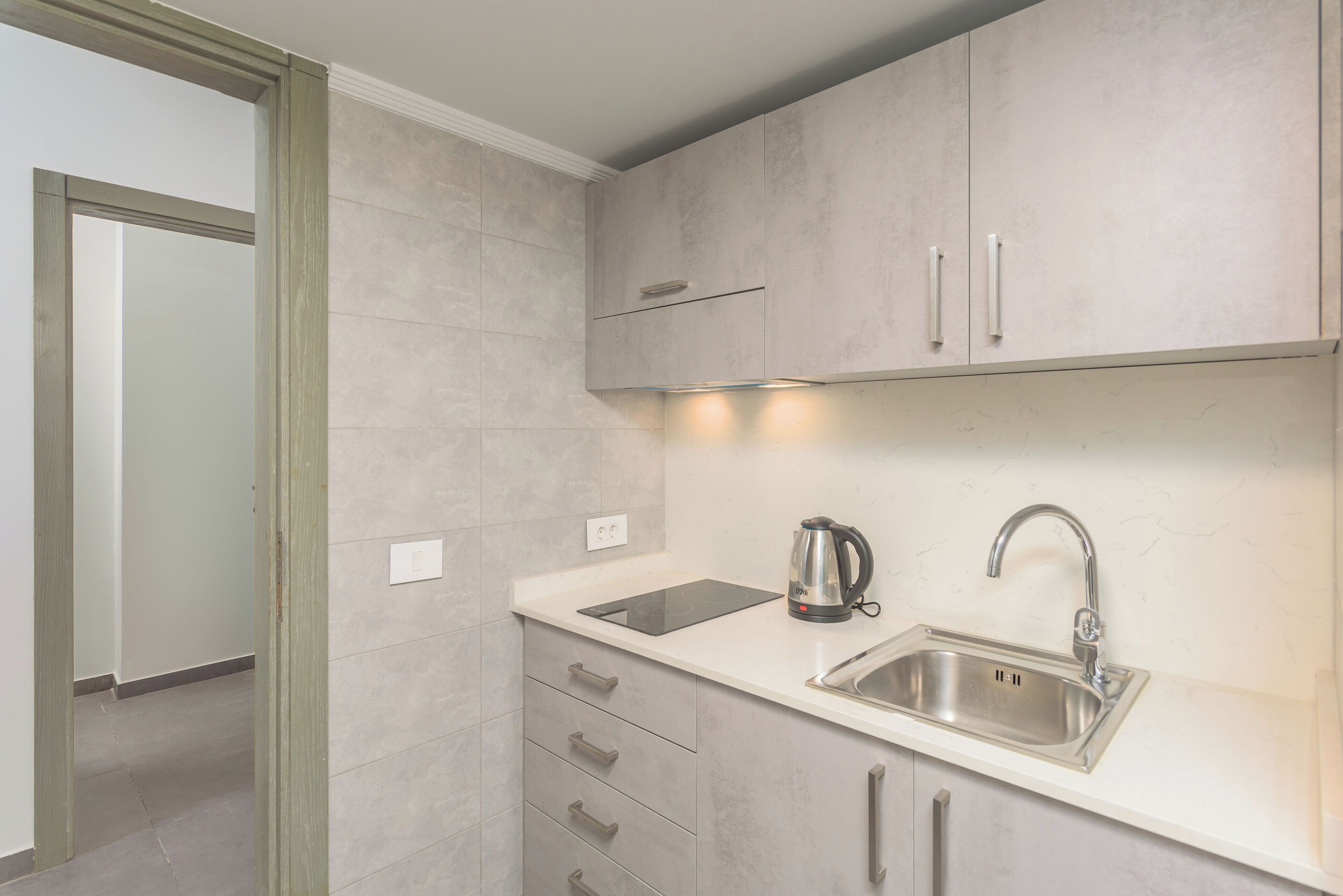 A modern kitchen with a built-in dishwasher, a stainless steel sink, and a kettle on the countertop.