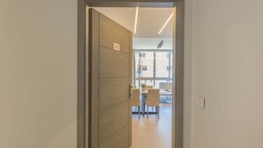 A modern interior with a wooden door marked "303", a dining area with a table and chairs, and a large window providing natural light. - Grey - Elegant Apartments in Awkar (Mazraet El Hadira)