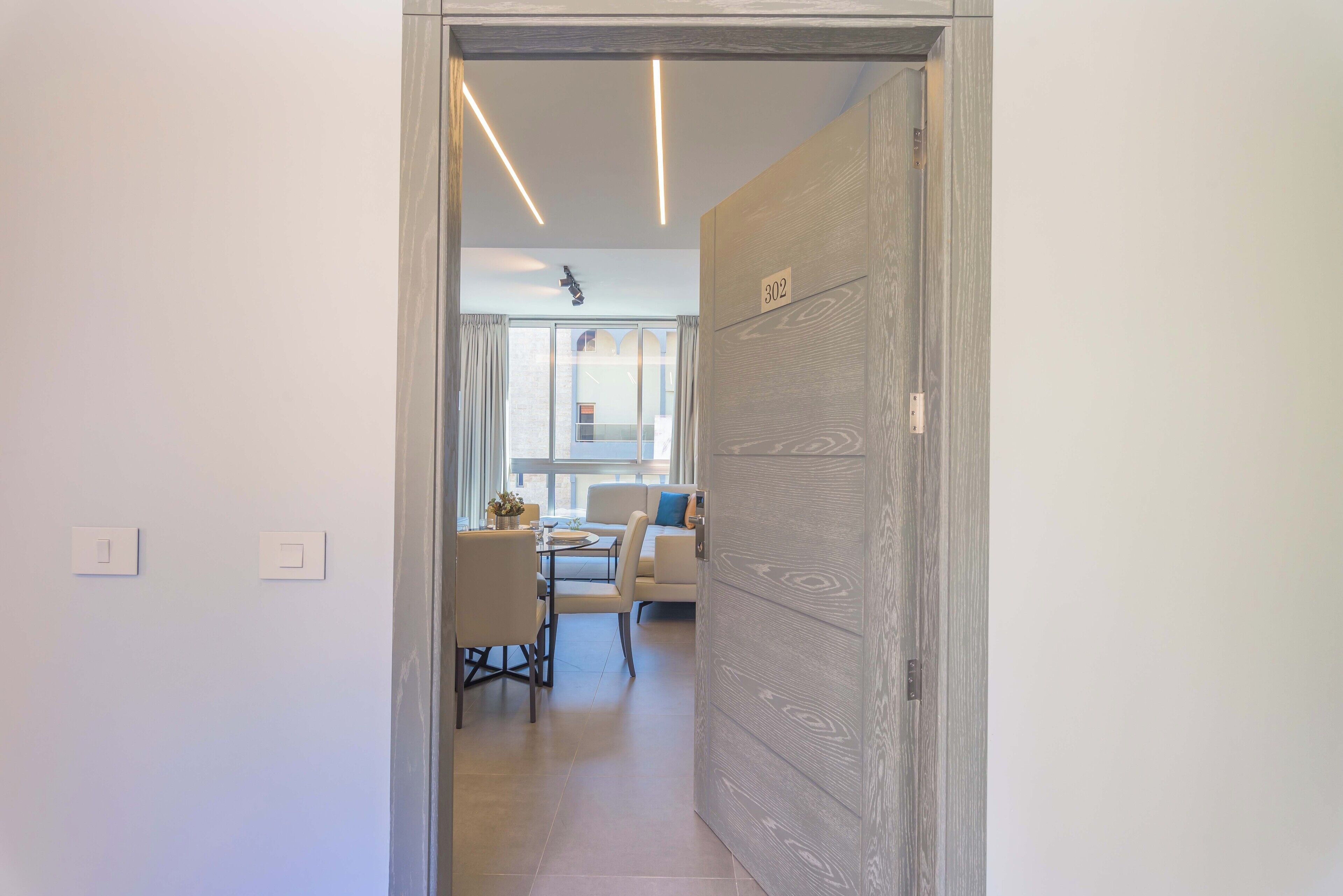 A hallway leading to a dining area with a table and chairs, a sofa, and a window with curtains.