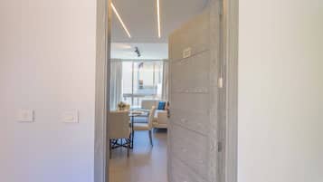 A hallway leading to a dining area with a table and chairs, a sofa, and a window with curtains.