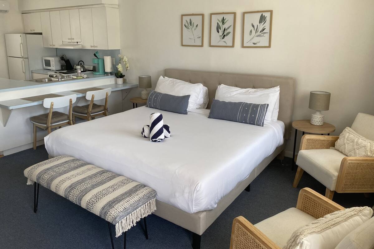 A hotel room with a bed, bedside tables, a desk, and a kitchenette.