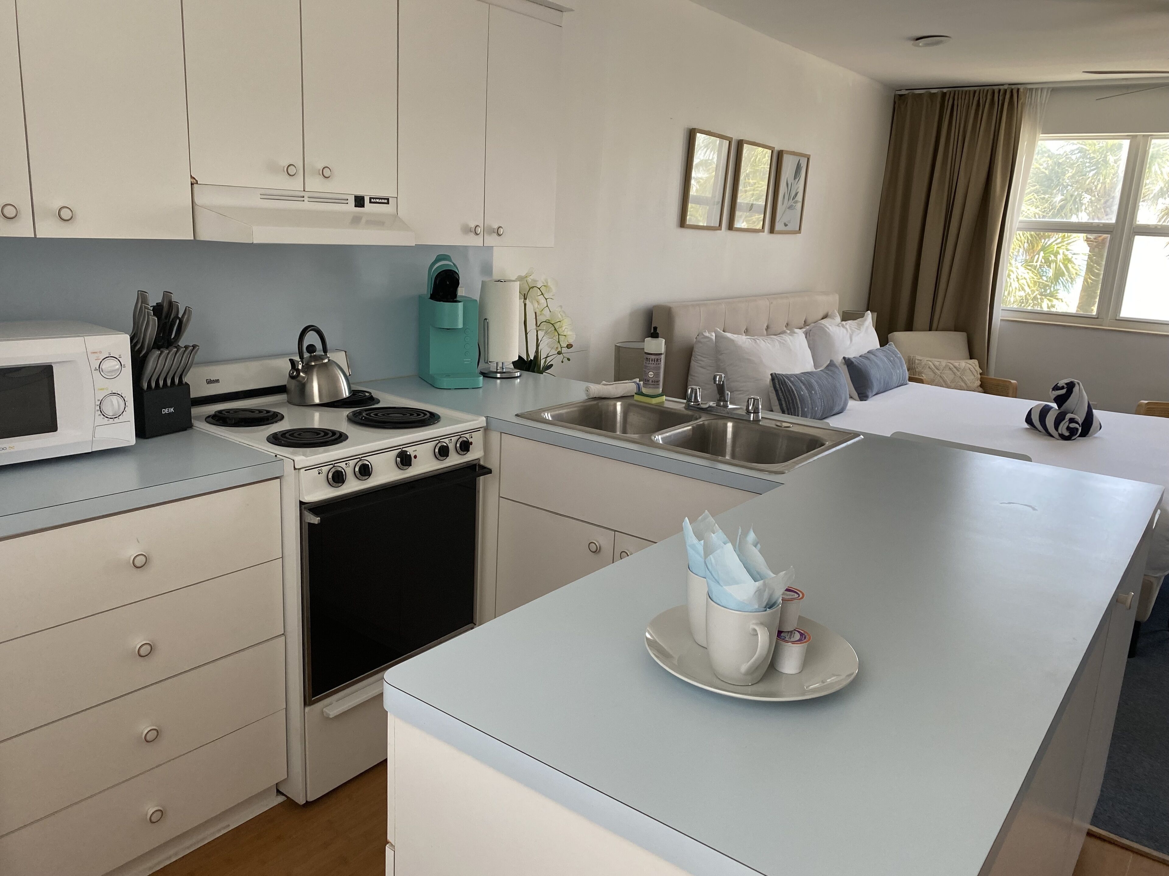 A modern kitchen with white cabinets, a stove, and a sink. There is a dining area with a table and chairs.