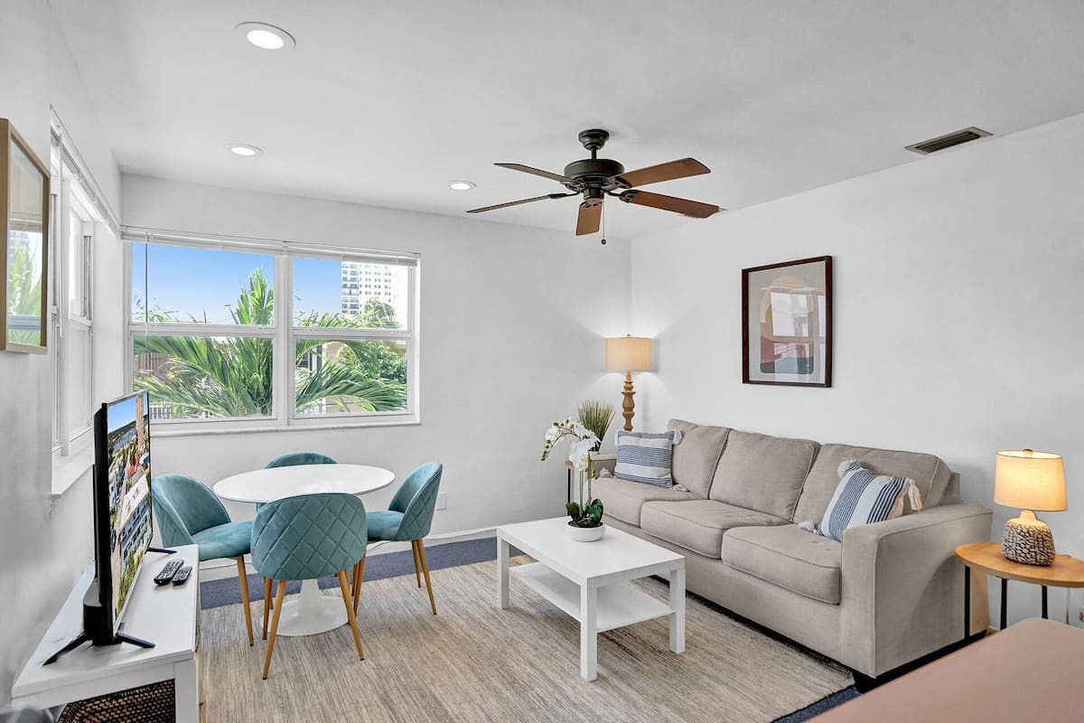A modern living room with a white sofa, teal chairs, a white coffee table, and a ceiling fan.