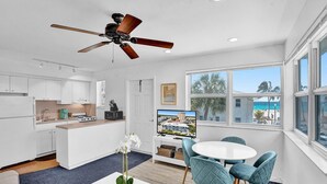 A modern kitchen with white cabinets, a built-in oven, and a toaster. There's a dining area with a round table and teal chairs. A ceiling fan is visible, and the room has large windows with a view of palm trees and a beach. - MARINE VILLAS HOLLYWOOD  (Hollywood)
