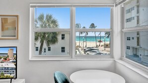 A room with a large window offering a view of a beach, a chair, and a table. - MARINE VILLAS HOLLYWOOD  (Hollywood)