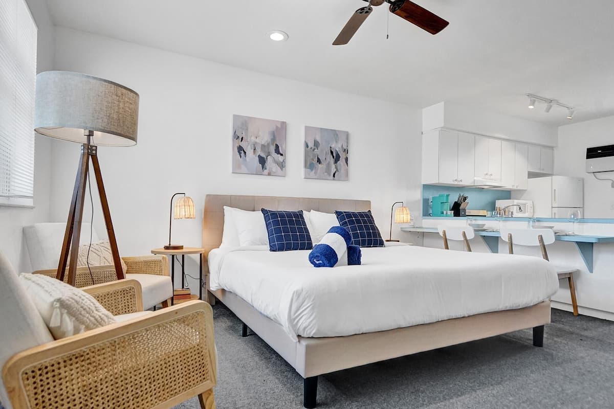 A modern hotel room with a large bed, a desk, and a kitchenette.