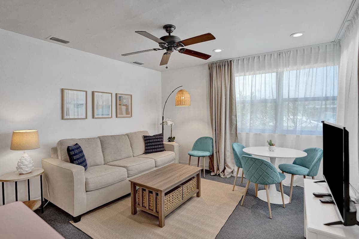A modern living room with a sofa, coffee table, and teal chairs around a small table.