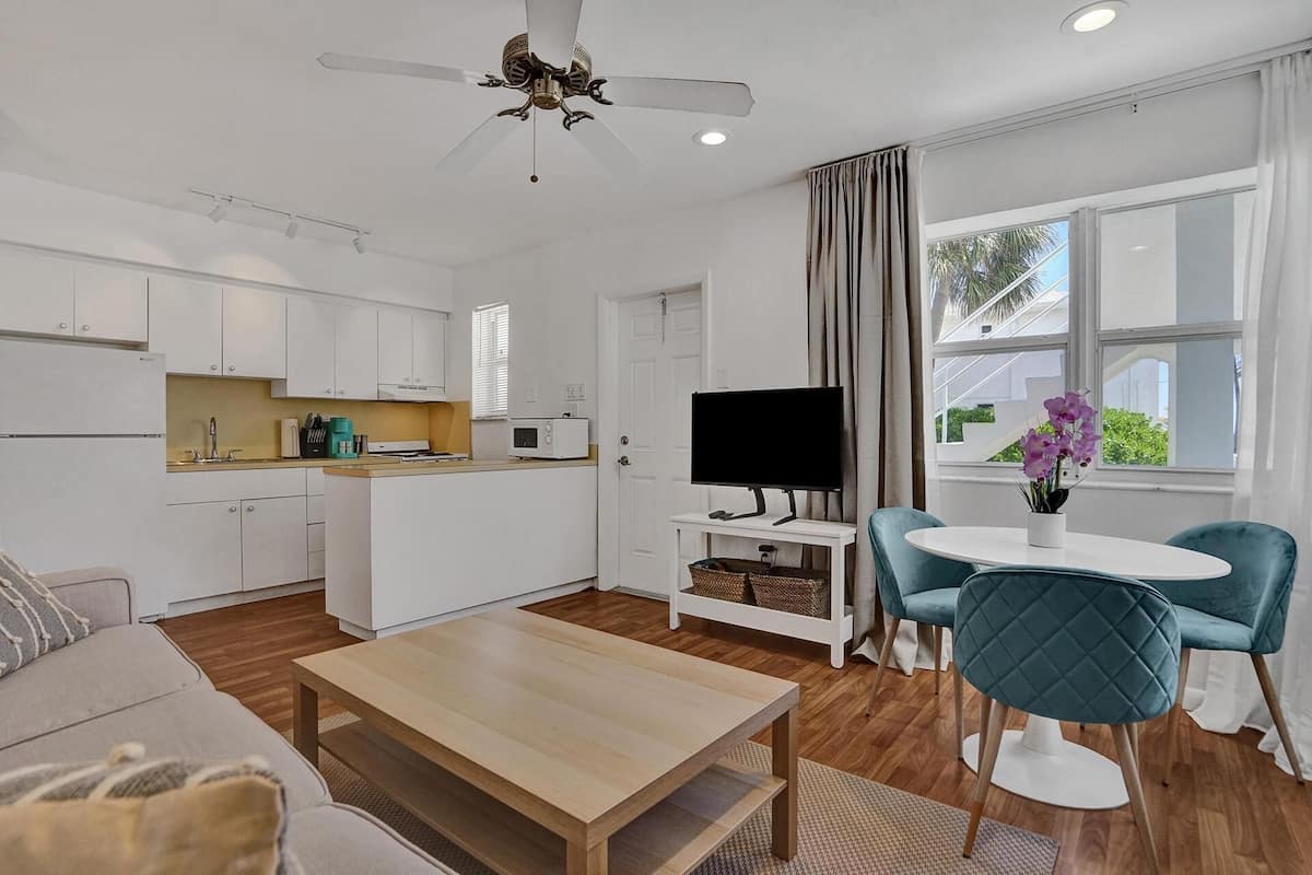 A modern apartment with a kitchenette, a dining area, a living room with a sofa and a coffee table, a TV, and a window with curtains.