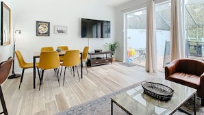 Een moderne woonkamer met een eethoek, een plafondventilator, een flatscreen televisie en grote schuifdeuren die uitkomen op een terras.