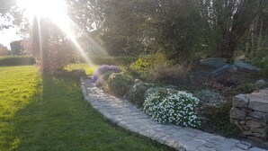 A garden pathway with stone borders, surrounded by lush greenery and flowering plants.